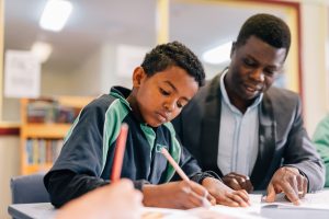 Picture of an adult next to a young person who is writing 