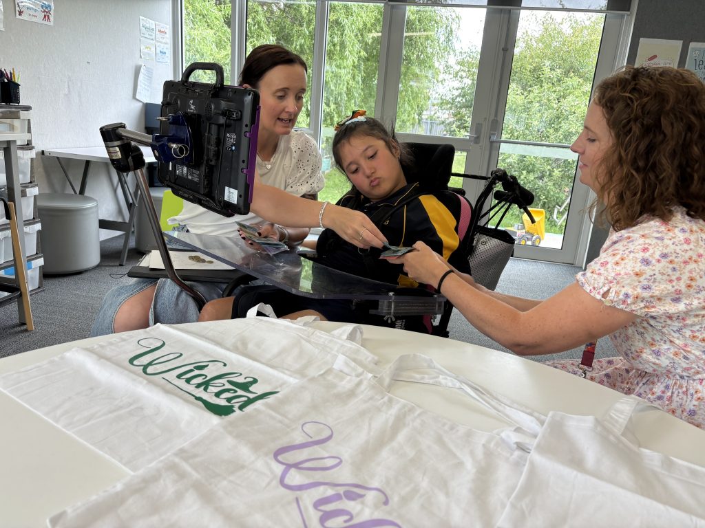 A girl in a wheelchair and two women, all counting money together.