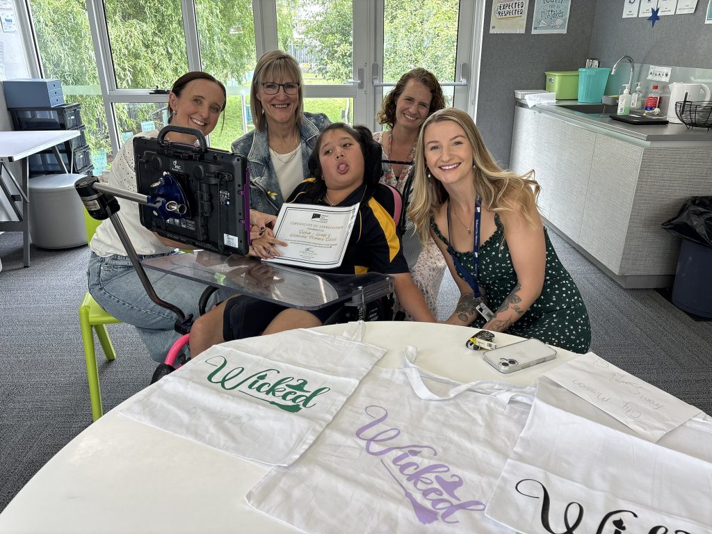 A girl in a wheelchair holding a certificate, surrounded by four women. 